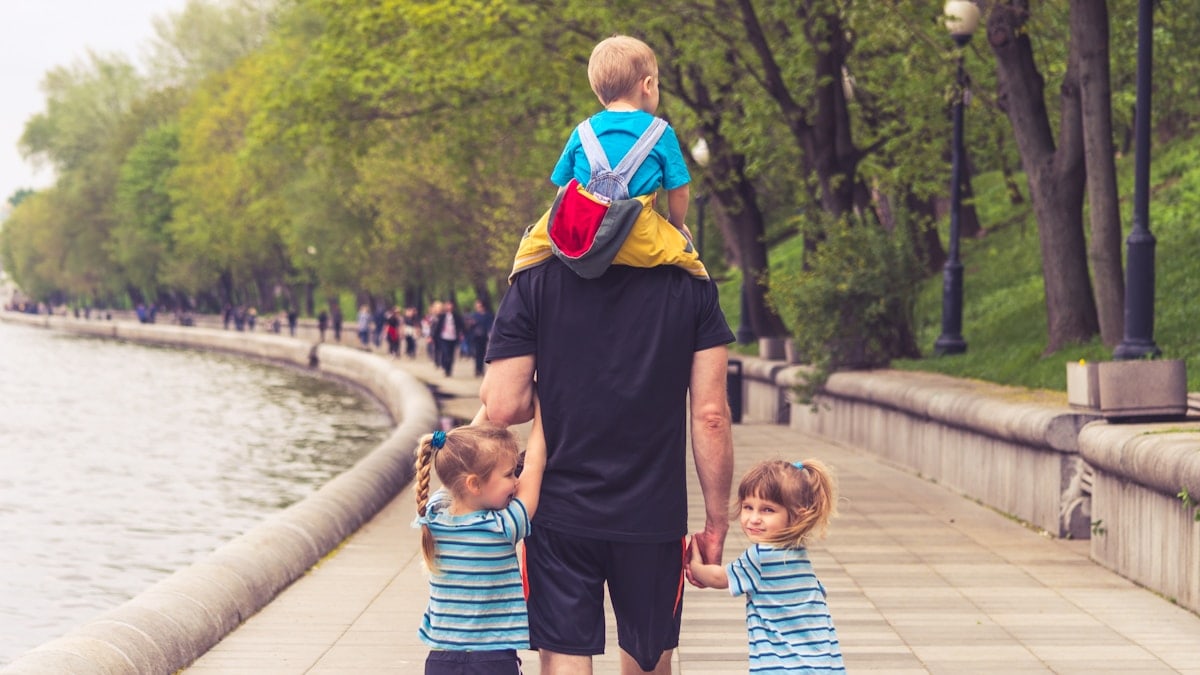 the father walks with three kids in the park