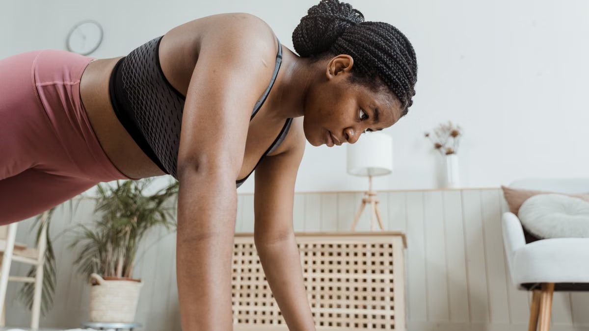 Woman with braided hair doing push-ups indoors, focusing on fitness and strength.